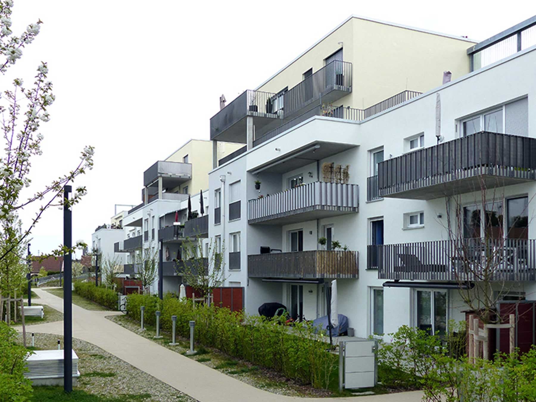 Foto eines Mehrparteienhauses, deren Gärten im Erdgeschoss zu einem Fußweg ausgerichtet sind.